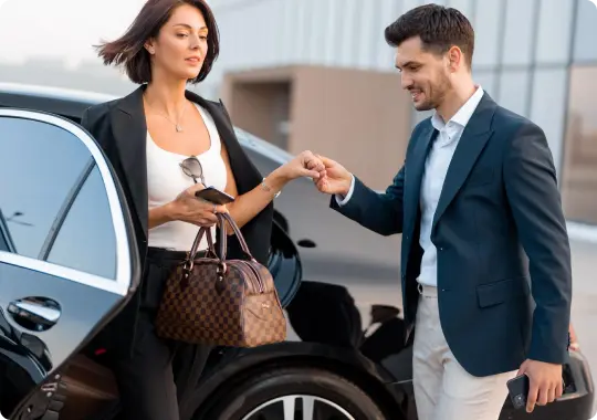 The chauffeur politely assists a businesswoman exiting a luxury car outside a modern terminal building.