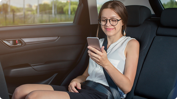 A woman in a white sleeveless top and black shorts scrolling her phone comfortably in a sunlit ride.