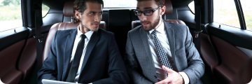 Two businessmen seated inside a luxury vehicle having a conversation during a ride.