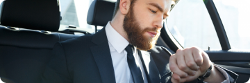 Bearded executive checking his wristwatch while seated in a car, symbolizing hourly chauffeured service.