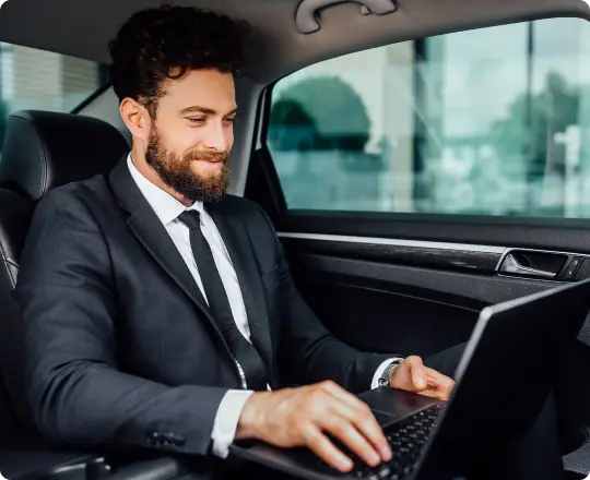 Business traveler working on a laptop in the backseat of a premium vehicle, highlighting comfort and productivity on the move.