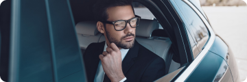 Stylish businessman in glasses looking out of a car window while adjusting his collar.