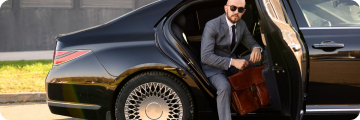 A man stepping out of a luxury car with a briefcase for a city-to-city transfer.