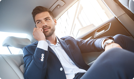 Confident businessman in a navy blue suit relaxing in the backseat of a luxury vehicle, smiling while talking on the phone