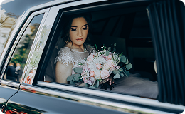 Bride holding a bouquet while seated inside a luxury wedding car.