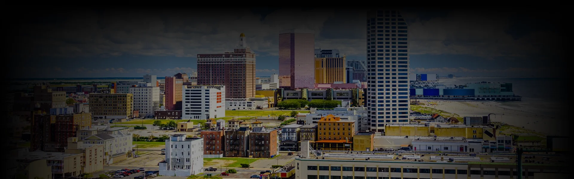 Chauffeur in a black suit opening the door of a black luxury sedan for a client in a cream-colored coat, photographed from above on a cobblestone driveway.